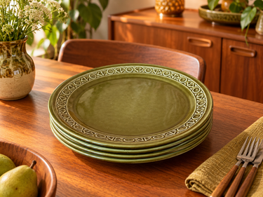 Five vintage Beswick Zorba olive-green plates stacked on a teak dining table in a retro interior