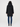 A person shown from the back wearing a black hooded coat with dark blue jeans and black ankle boots, standing against a plain light gray studio background.