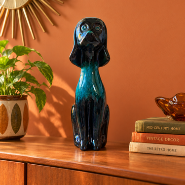 Vintage Blue Mountain Pottery sitting dog in green and blue glaze on a wooden sideboard against a warm terracotta wall