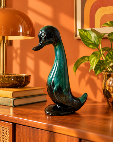 Vintage green Blue Mountain Pottery sitting duck displayed on a wooden cabinet against a burnt orange wall