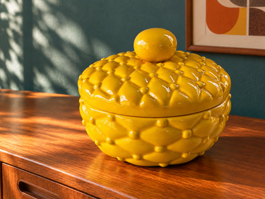 Vintage 1979 mustard yellow ceramic quilt-pattern trinket dish with lid, styled on a teak sideboard against a teal wall.