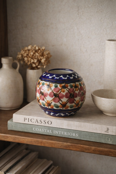 Decorative ceramic vase with a geometric pattern on a shelf with books and other items.