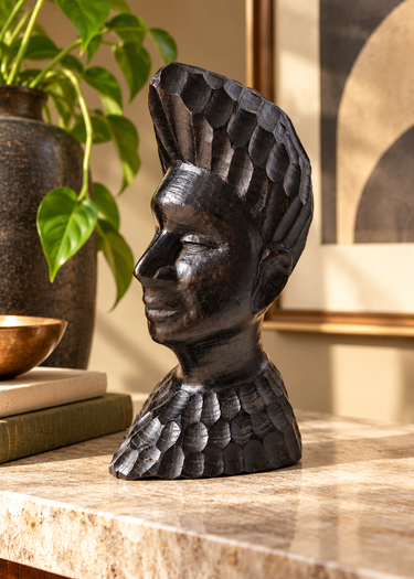 Vintage Tanzanian carved ebony male bust displayed on a pale stone surface in a mid-century interior with greenery and warm natural light.